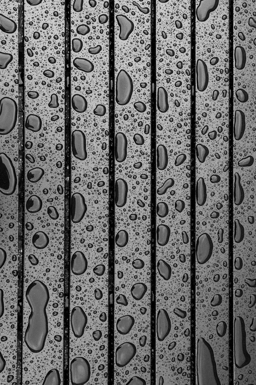 Raindrops forming droplets on a black table with vertical lines.