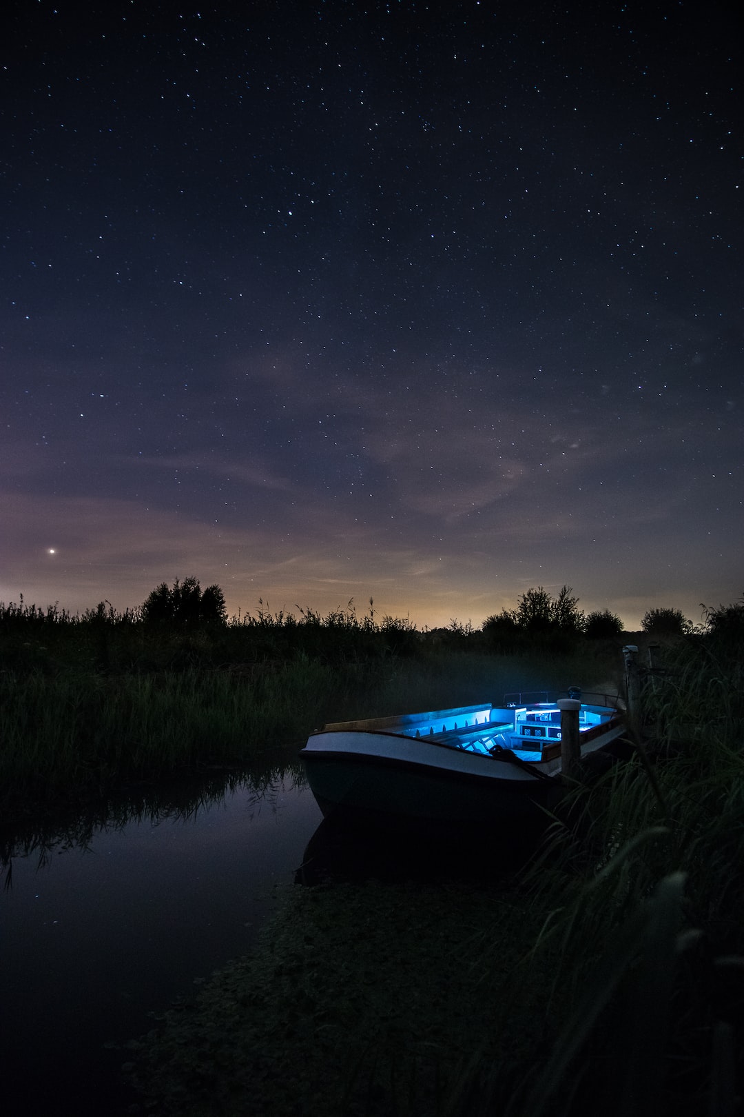 A boat is tied to the dock under a starry nights’ sky.