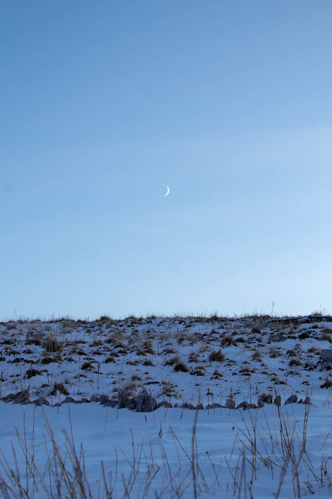 Moon in the clear blue sky with dune covered with snow