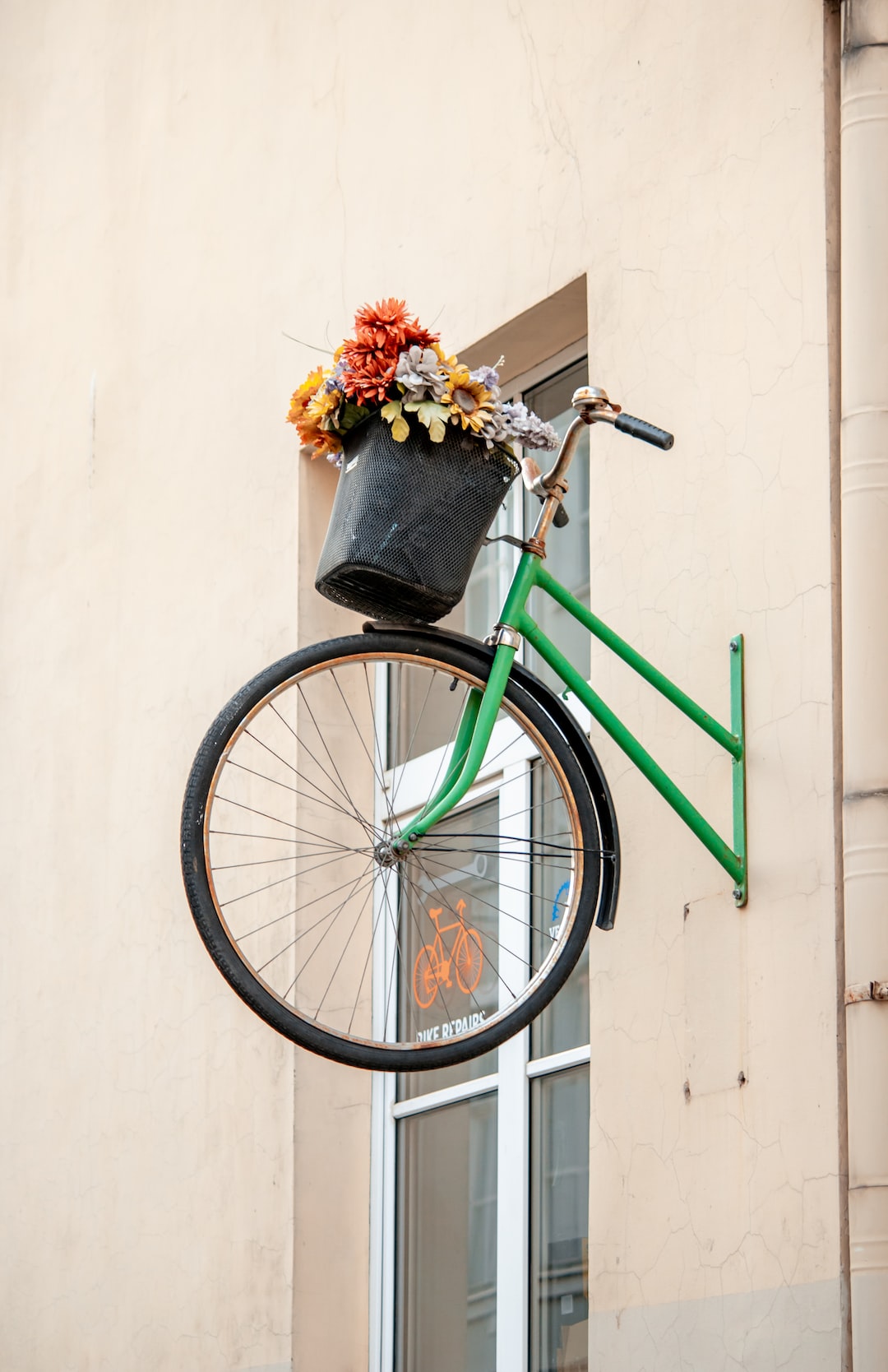 decorative bicycle with a basket of flowers mounted on the wall of the house. the front of the bike on the front of the house