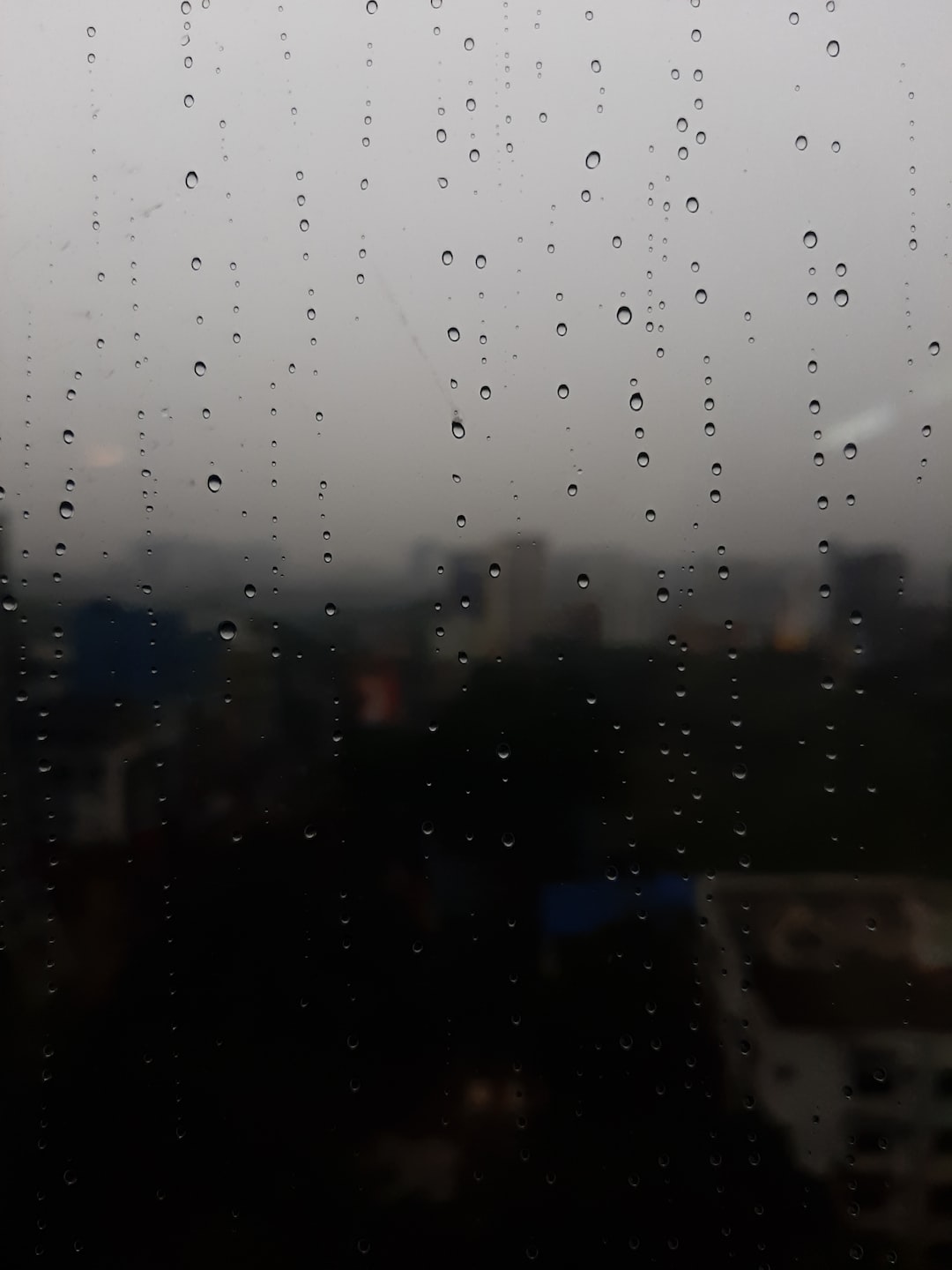 Raindrops on glass in a rainy day with dark background