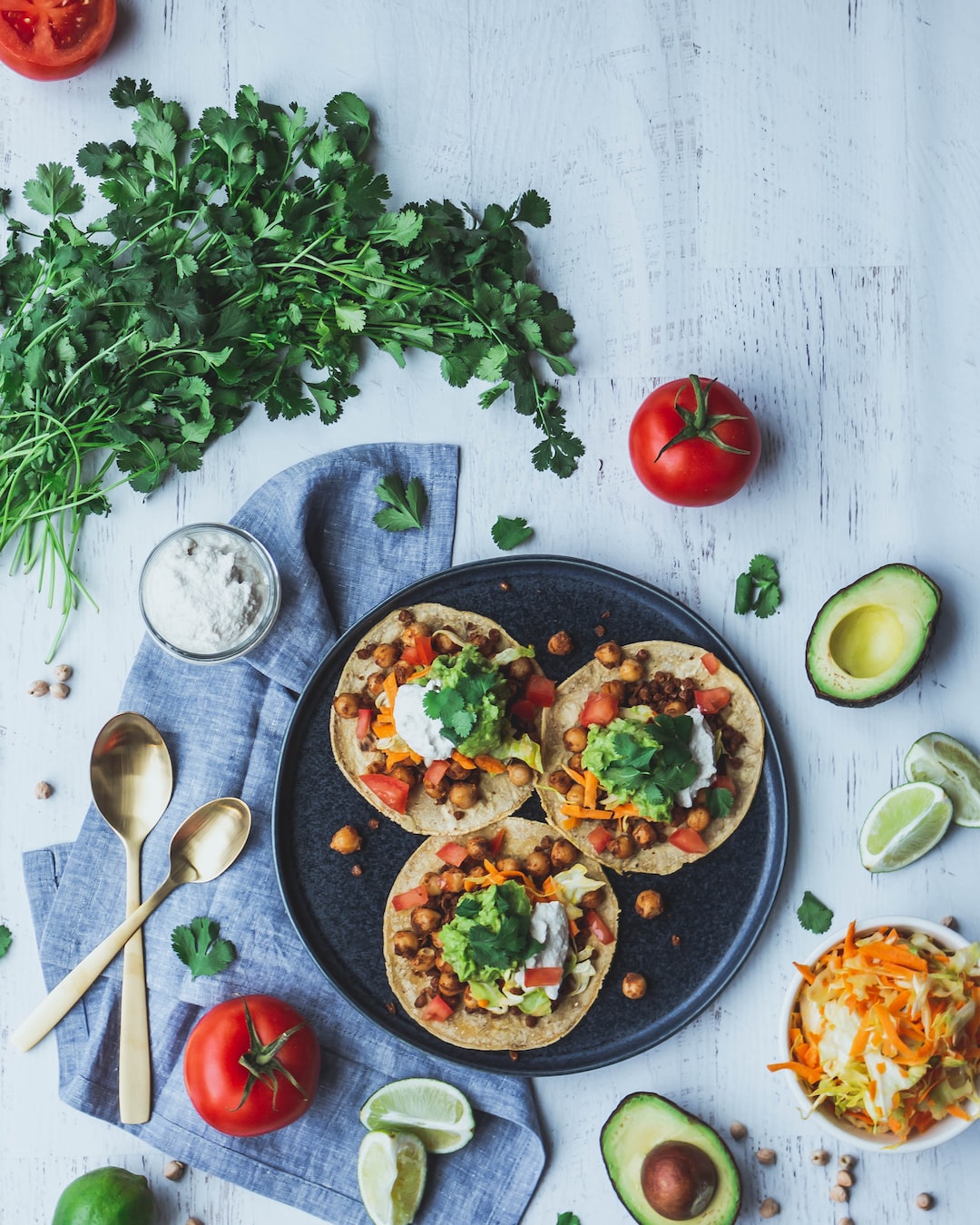 Vegan chickpea and lentil tacos. Flat lay style food photography. Scene includes cilantro, avocados, tomatoes, and limes.