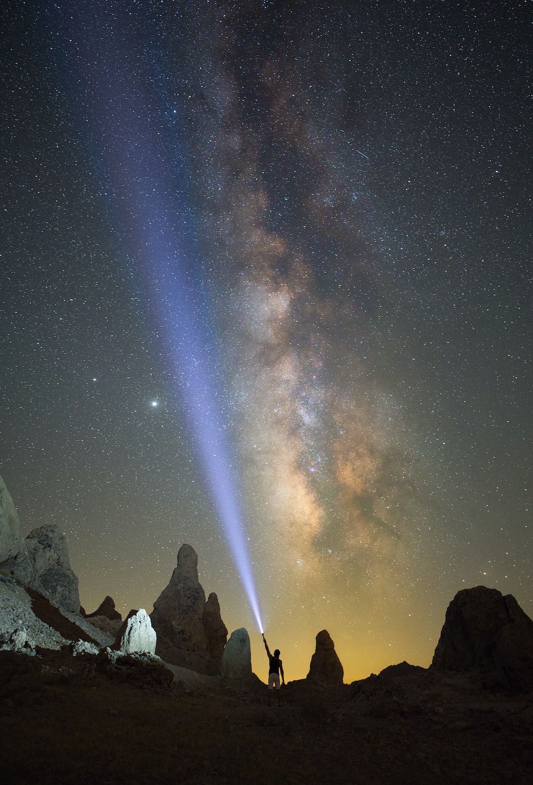 A man holds a flashlight to a star lit sky in the desert. 