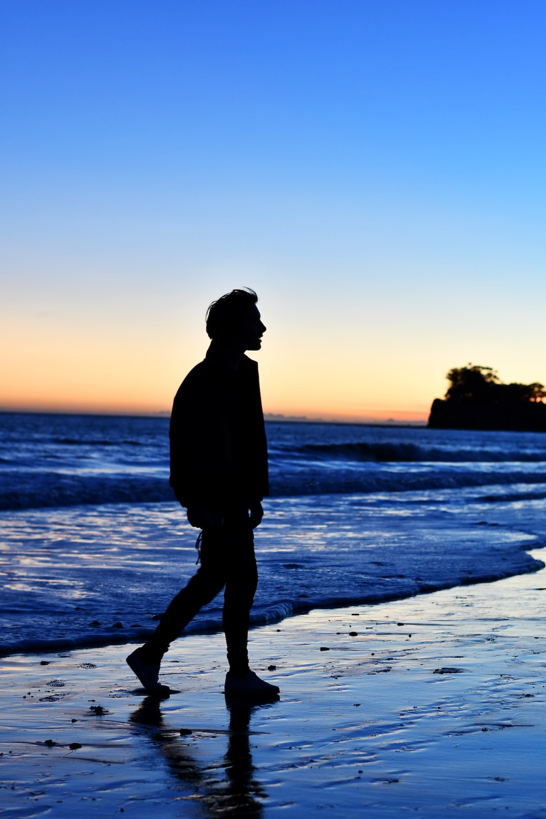 A man walking down the beach at sunset