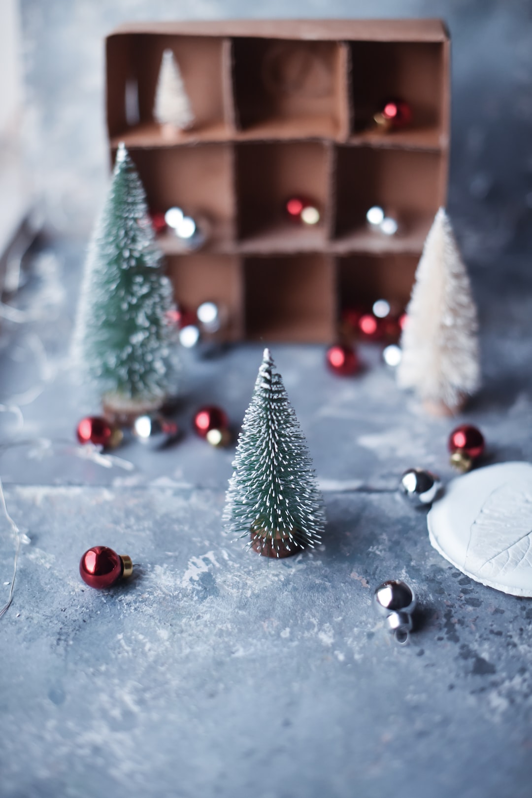 Christmas miniature trees still life with gift box of baubles. On a grey background.