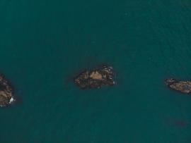 Top down drone photograph of rocks in blue water