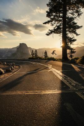 Silhouette of a man jumping in Yosemite National Park during a beautiful sunrise on Glacier Point with Half Dome in the background.