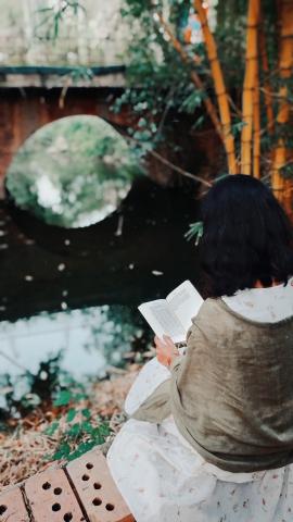 A Girl holding book, sitting by the side of canal and living her fantasy
