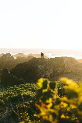 A couple of friends taking photos of the pacific ocean from a rocky outcrop on the shoreline in Ucluelet, BC, Canada.