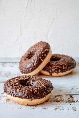 Donuts with chocolate glazing and chocolate sprinkles on kitchen table