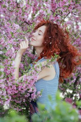 Tender and aesthetic portrait of a redheaded girl in pink flowers close-up. Sensual young girl posing sideways to the camera.