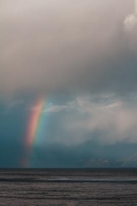 Rainbow over ocean with mountain range