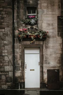 White vintage door on the front of a house with flowers adorning the window in the city of Edinburgh, Scotland.