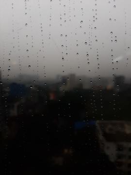 Raindrops on glass in a rainy day with dark background