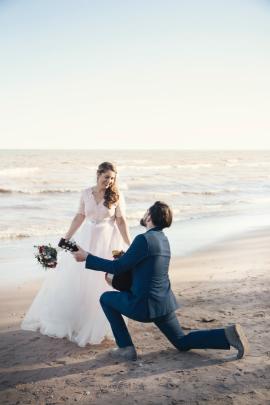 Bride and groom on beach with groom on bended knee with guitar signing a song he wrote for his bride