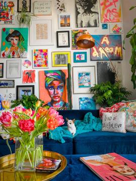 Tiny chihuahua on blue velvet couch in front of a colorful maximalist gallery wall in a Denver apartment home with lots of plants and flowers