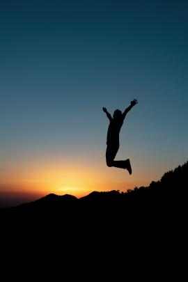 A silhouette of jumping person during sunset in mountains.