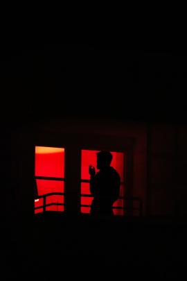 A man is smoking a cigarette on his balcony at night.
