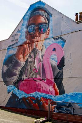 A mural of a man with sunglasses blowing up a pink inflatable flamingo.