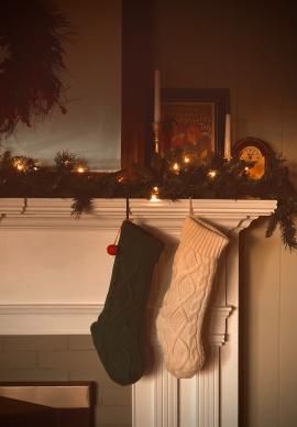Knitted Christmas Stockings hanging from a fireplace mantle adorned with lighted Christmas garland.