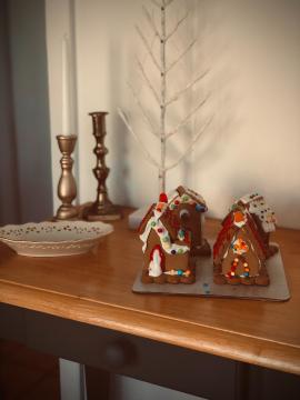 Poorly - but enthusiastically - decorated holiday gingerbread houses displayed in front of golden taper candles and a birch tree inspired winter decoration.