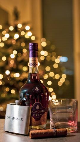 A bottle of a very nice cognac with a glass and a cigar and xmas tree behind. 