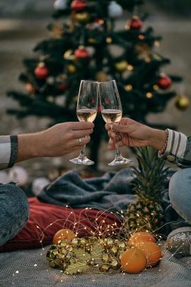 the hands of a man and a woman hold glasses on the background of a Christmas tree