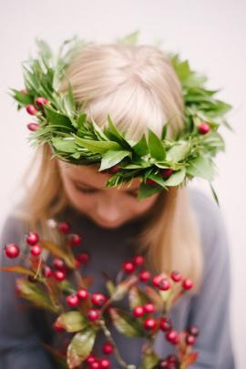 A five year old blonde girl holding holly and wearing a Christmas flower crown. It is a soft focus image that would make for a good Xmas card. 