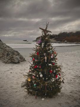 A Christmas tree sitting on a beach covered in ornaments.