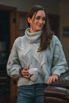 Woman drinking coffee, wearing a cozy sweater.