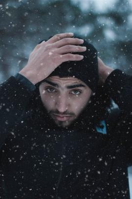 portrait of a man while he adjusts his beanie in cold winter while snow is falling