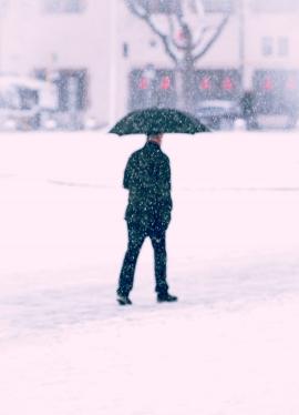 Older man is walking through strong snow fall with an umbrella through the city of Stuttgart, Germany