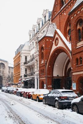 Parked cars in front of a red brick church contrasted by the white snow in winter in Berlin, Germany