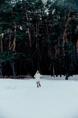 Woman running across snowy field by the forest. Winter seasonal aesthetics.