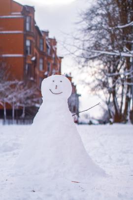 Snowman with twig arms in front of housing