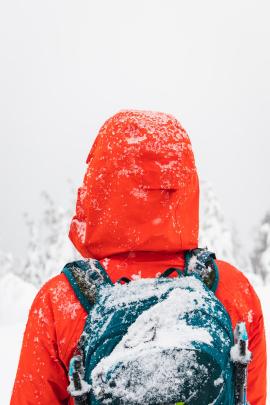 person wearing red winter jacket and backpack covered in snow