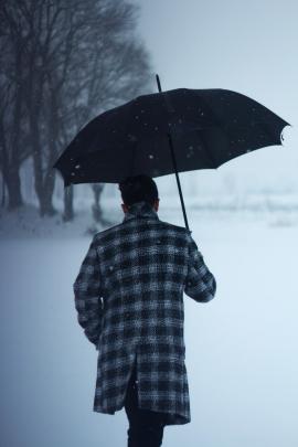 a guy walking with umbrella during a snowfall