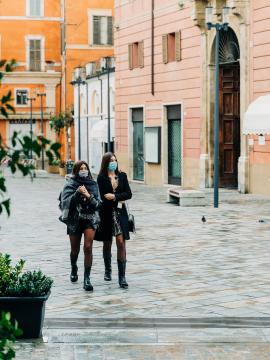 Two trendy girls, wearing face masks, cross a piazza in Rieti, Italy