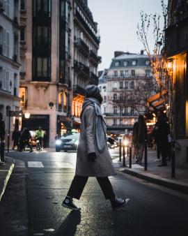 A girl crossing the street in Paris on a cold evening.